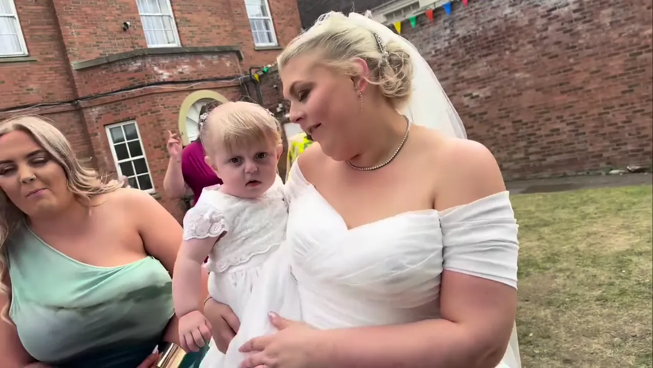 Bride holding a baby in white on the lawn
